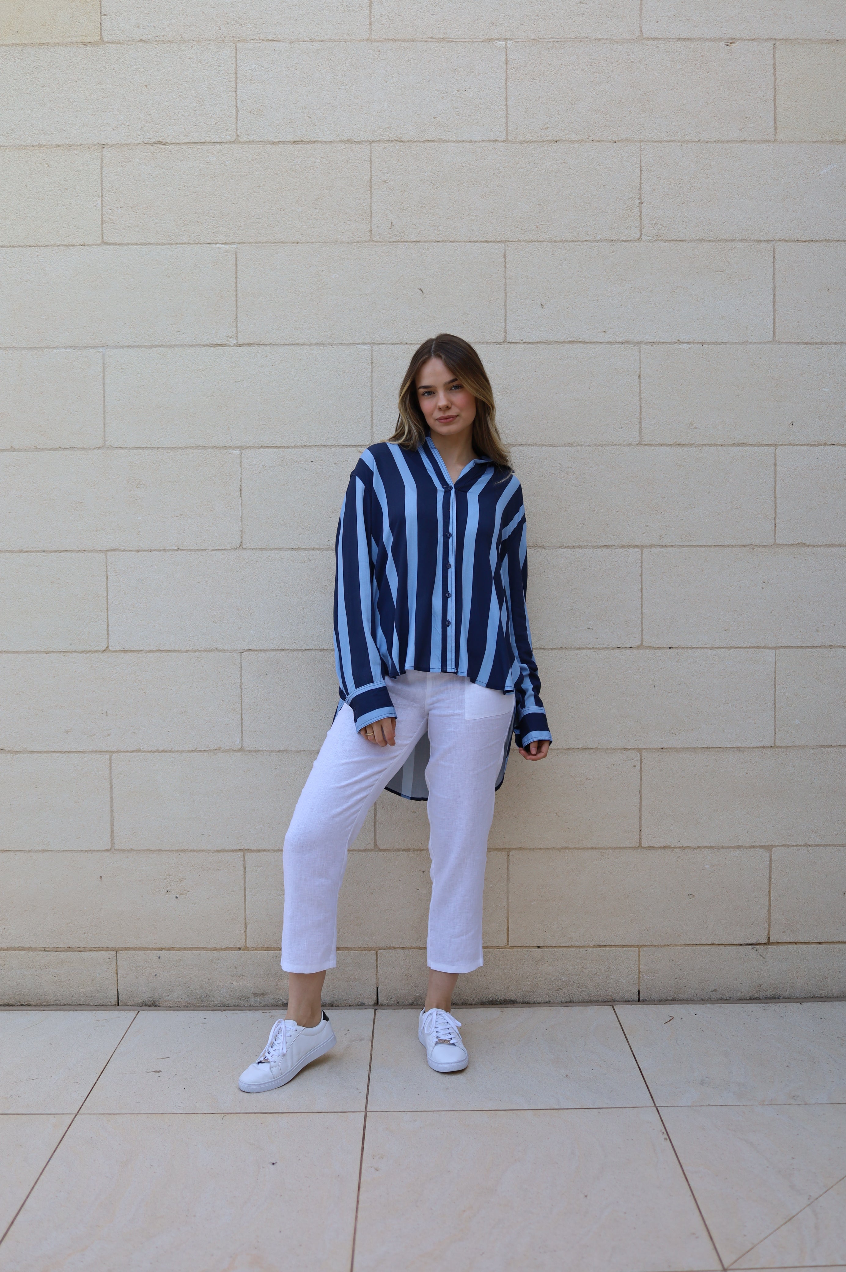 full length front view. Apre stripe shirt features, super draping rayon fabric, 2 tone thick stripe pattern in navy and light blue, button through front, button down cuff, curved hem with longer tail. 