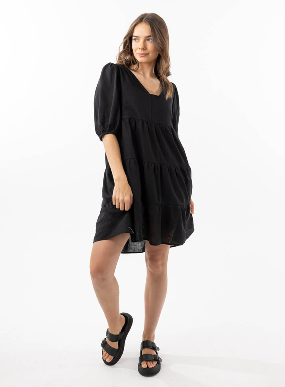 The Eleanor mini dress in black features a flowing layered a line shape with draping linen/viscose fabric, puff 3/4 sleeves with elastic cuff which can be pushed up to the elbow, a dropped v shape neckline with a square finish.