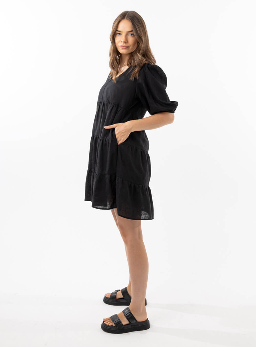 The Eleanor mini dress in black features a flowing layered a line shape with draping linen/viscose fabric, puff 3/4 sleeves with elastic cuff which can be pushed up to the elbow, a dropped v shape neckline with a square finish.