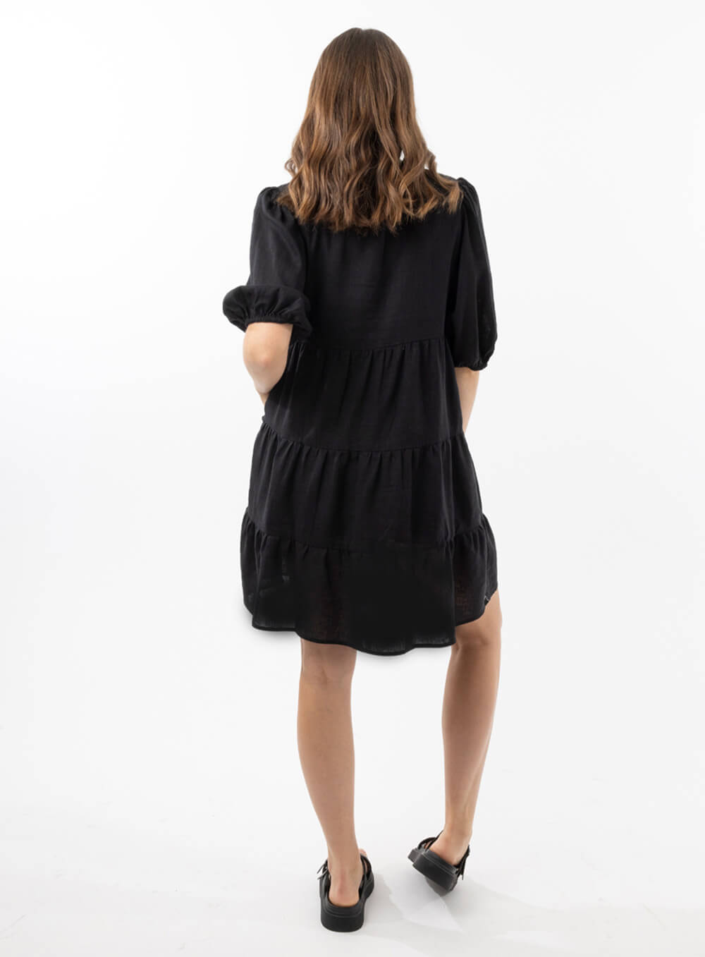 The Eleanor mini dress in black features a flowing layered a line shape with draping linen/viscose fabric, puff 3/4 sleeves with elastic cuff which can be pushed up to the elbow, a dropped v shape neckline with a square finish.