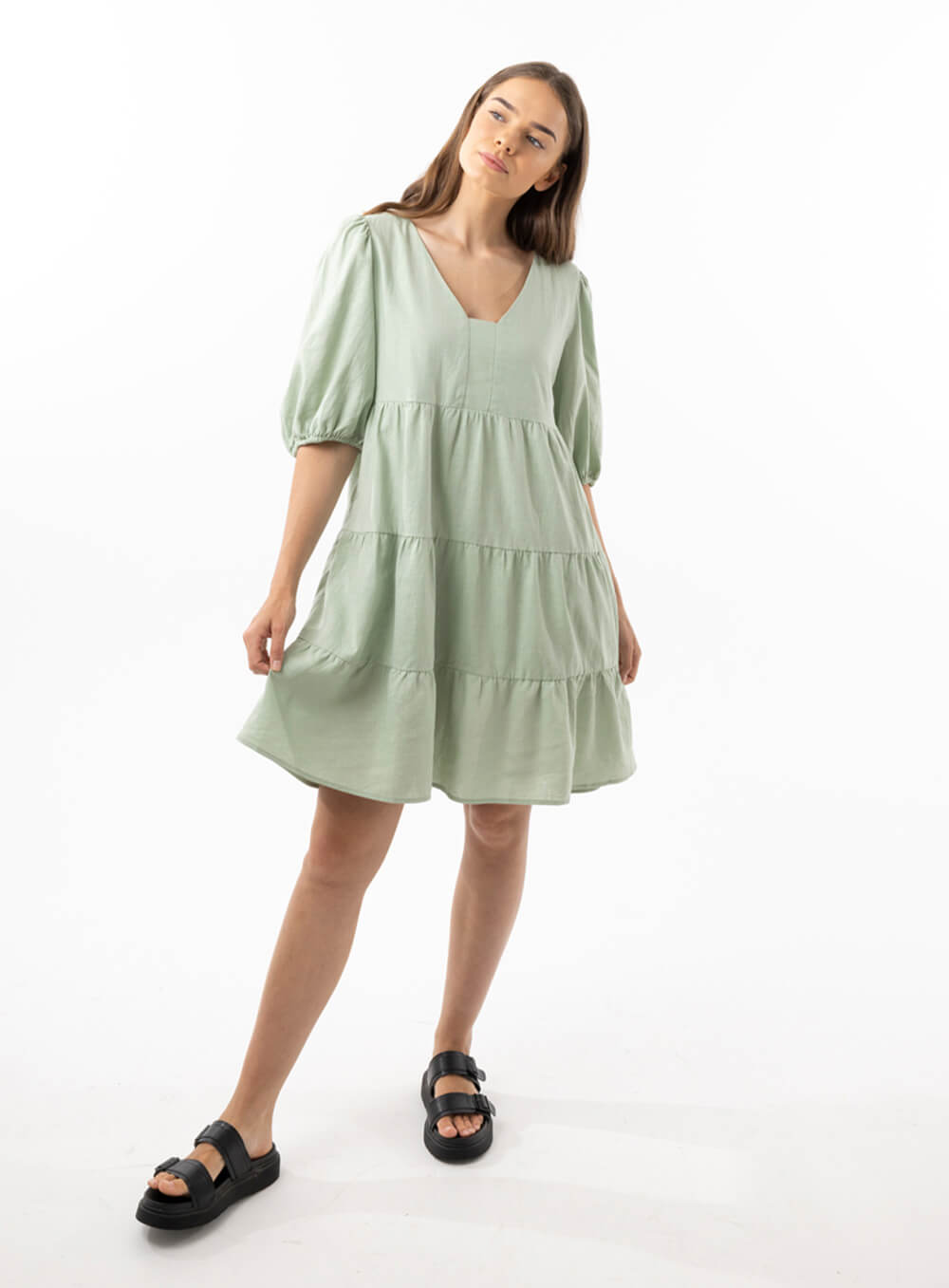 The Eleanor mini dress in sage features a flowing layered a line shape with draping linen/viscose fabric, puff 3/4 sleeves with elastic cuff which can be pushed up to the elbow, a dropped v shape neckline with a square finish.