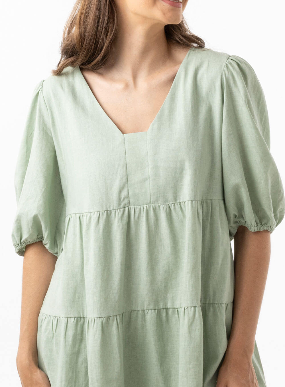 The Eleanor mini dress in sage features a flowing layered a line shape with draping linen/viscose fabric, puff 3/4 sleeves with elastic cuff which can be pushed up to the elbow, a dropped v shape neckline with a square finish.