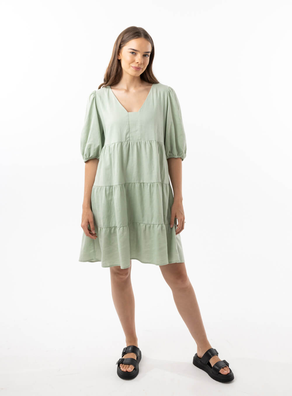 The Eleanor mini dress in sage features a flowing layered a line shape with draping linen/viscose fabric, puff 3/4 sleeves with elastic cuff which can be pushed up to the elbow, a dropped v shape neckline with a square finish.