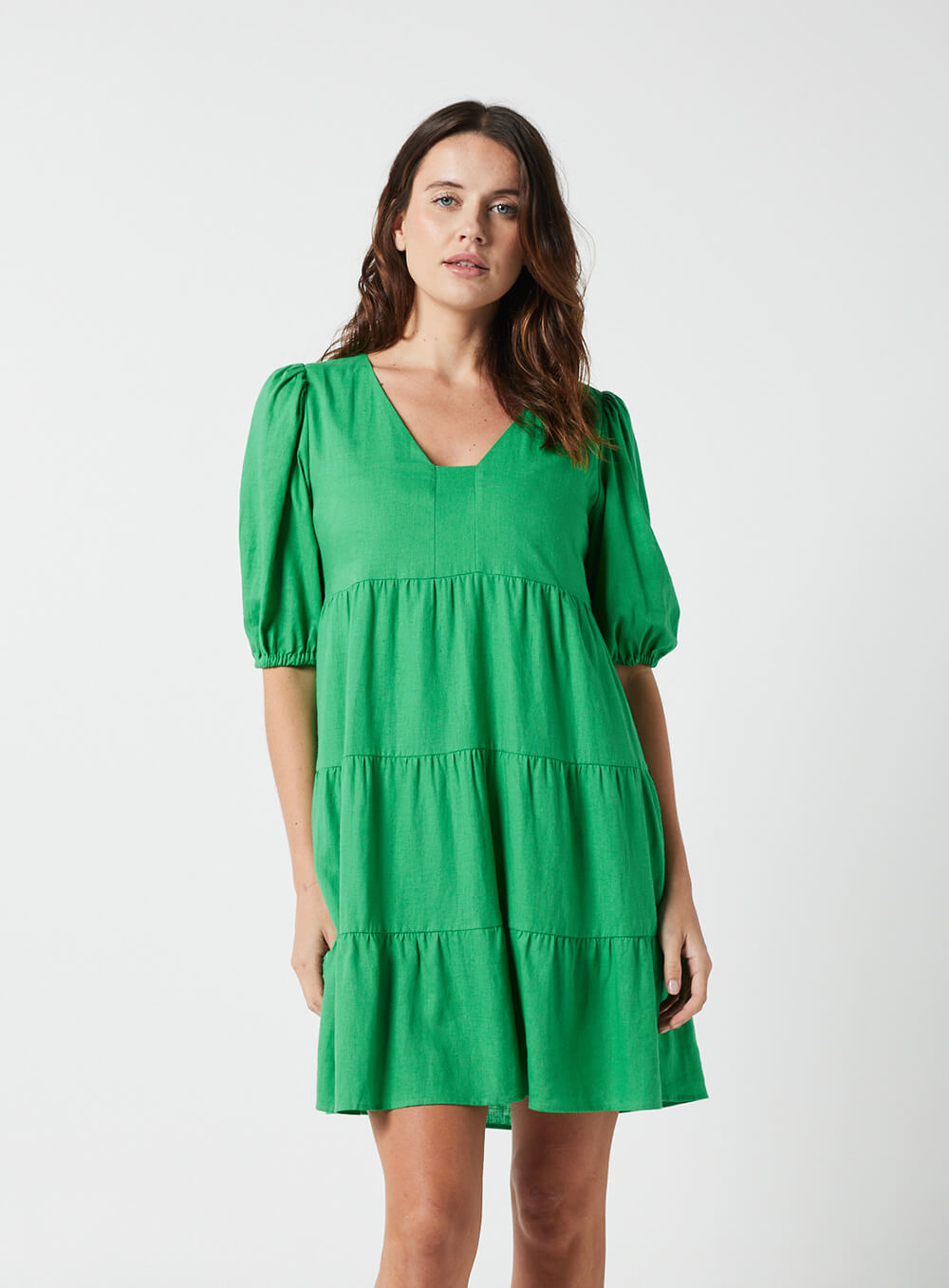 The Eleanor mini dress in green features a flowing layered a line shape with draping linen/viscose fabric, puff 3/4 sleeves with elastic cuff which can be pushed up to the elbow, a dropped v shape neckline with a square finish.